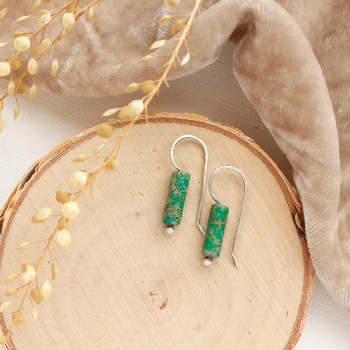 The green sediment jasper lobe hugger earrings styled on wood with tan velvet and dried grass.