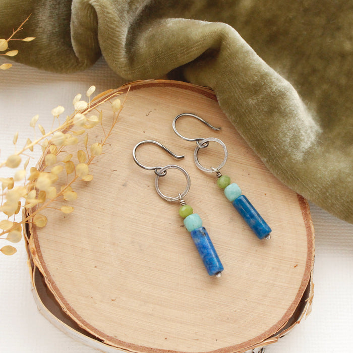 The cobalt sydney hoop earrings styled on wood with green velvet and dried grass.
