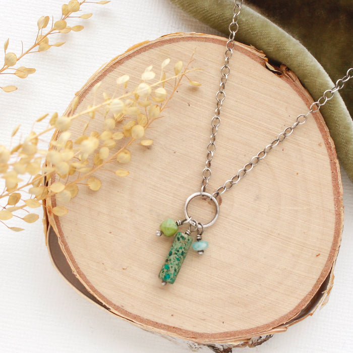 The meadow sydney charm necklace styled on wood with green velvet and dried grass.