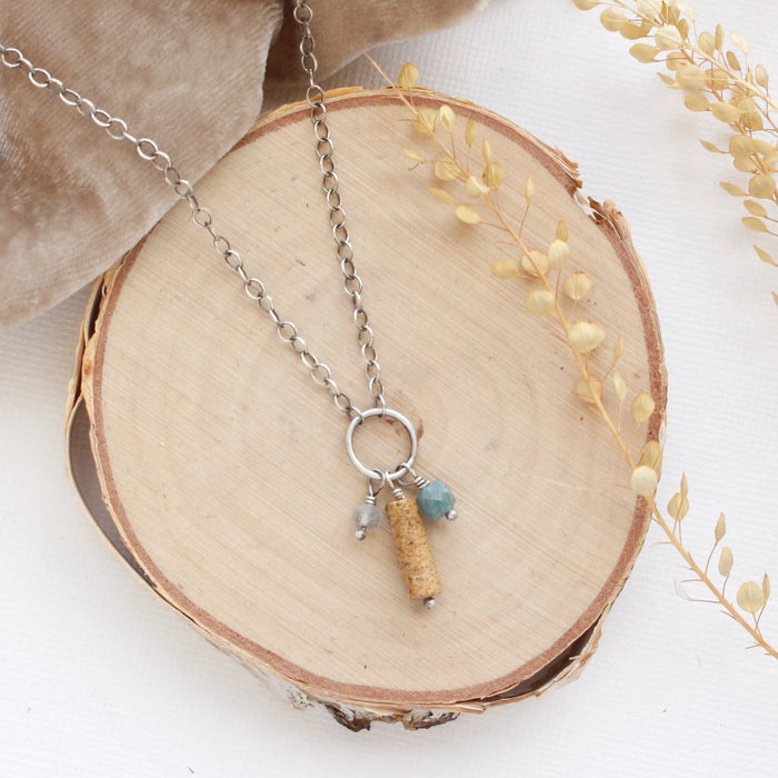 The oasis sydney charm necklace styled on wood with tan velvet and dried grass.