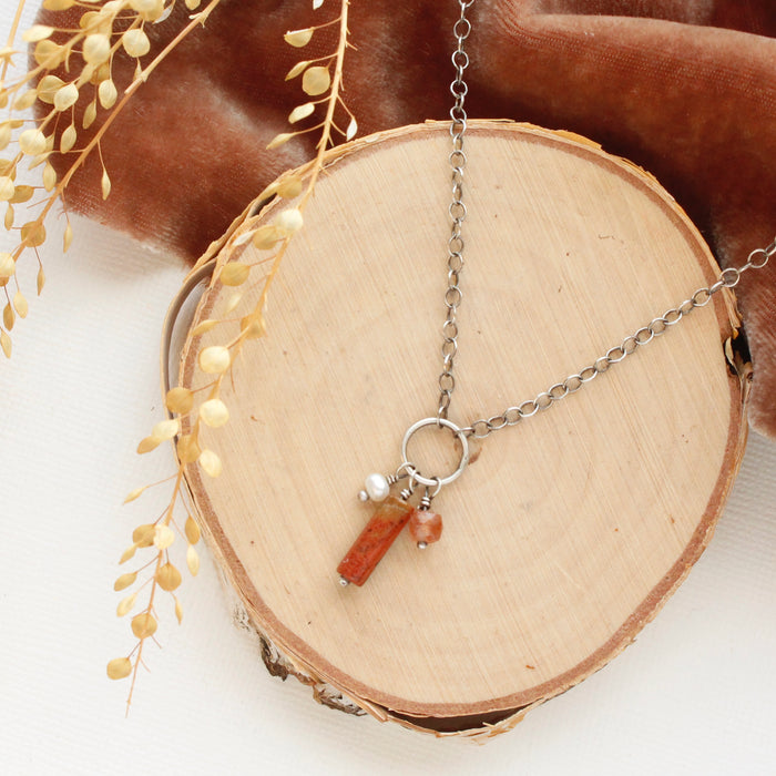 The canyon sydney charm necklace styled on wood with orange velvet and dried grass.