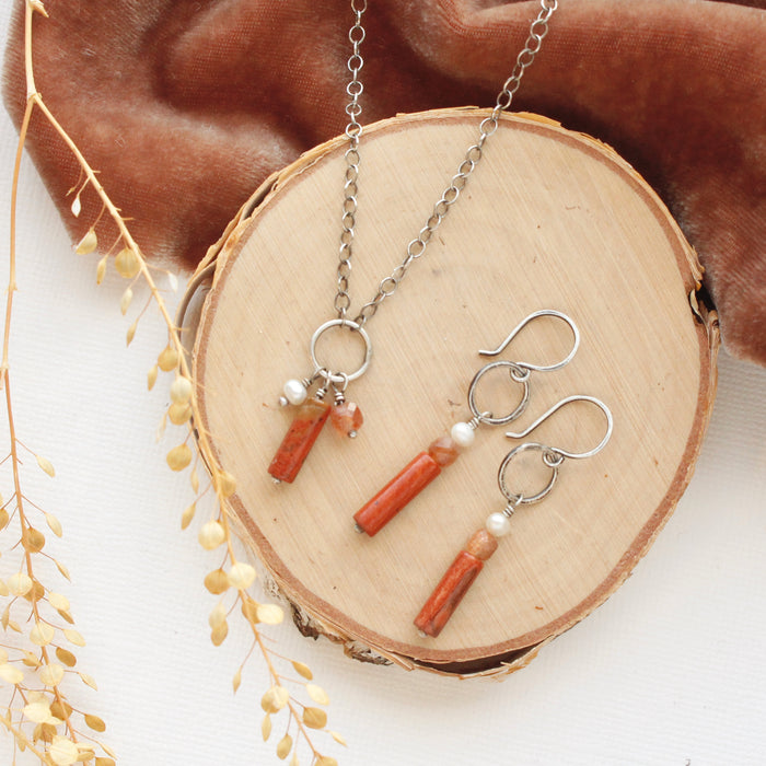 The canyon sydney hoop earrings and matching necklace styled on wood with orange velvet and dried grass.