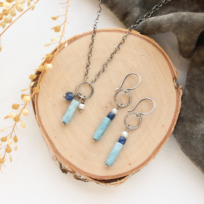 The mirage sydney hoop earrings and matching necklace styled on wood with gray linen and dried grass.