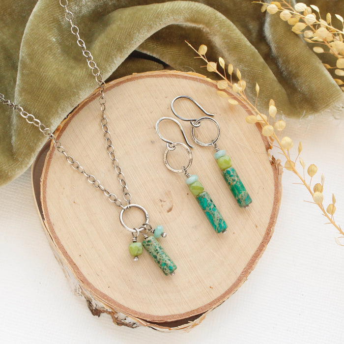 The meadow sydney hoop earrings and matching necklace styled on wood with green velvet and dried grass.