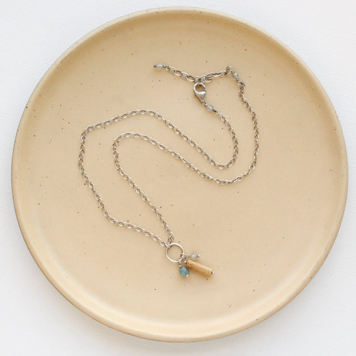 The oasis sydney charm necklace styled on a tan plate to show the adjustable lobster clasp closure.