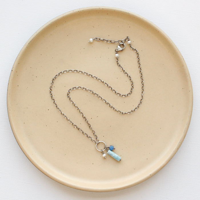 The mirage sydney charm necklace styled on a tan plate to show the adjustable lobster clasp closure.