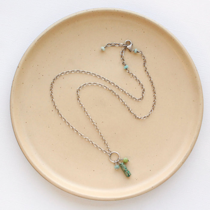 The meadow sydney charm necklace styled on a tan plate to show the adjustable clasp closure.