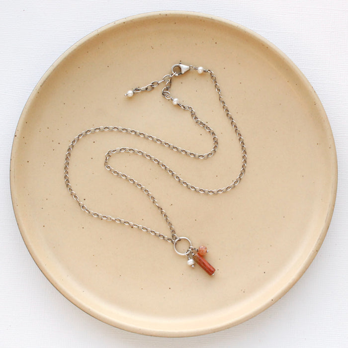 The canyon sydney charm necklace styled on a tan plate to show the adjustable lobster clasp closure.