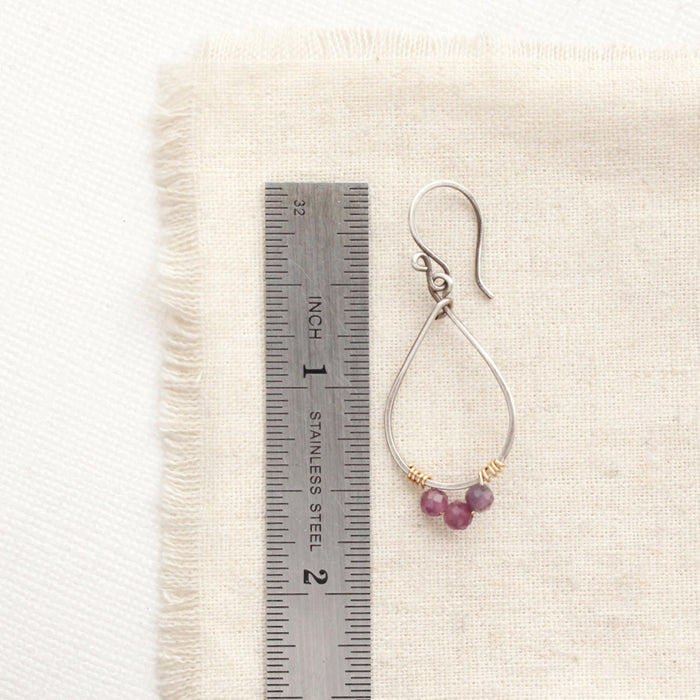 A purple ruby wrapped teardrop hoop earring next to a ruler for size reference