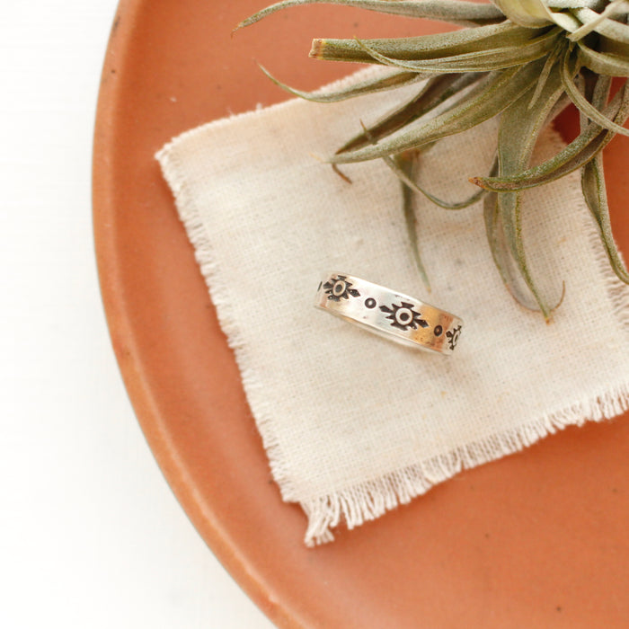 The stamped reno ring styled on a red plate with tan linen and an air plant