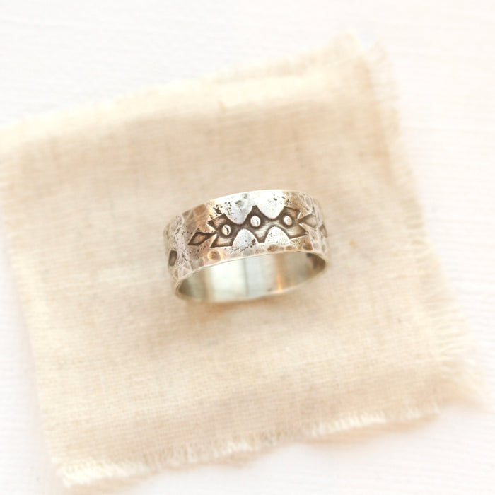 A rustic stamped silver ring styled on tan linen