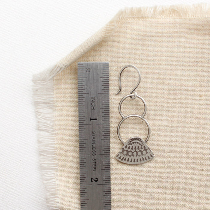 An asmi triangle double loop earring next to a ruler for size reference