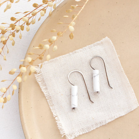 The sydney white howlite lobe hugger earrings styled on a tan plate with linen and dried grass