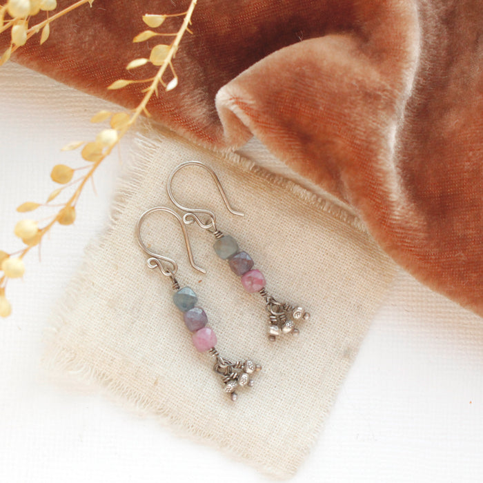 The stacked sapphire dangle earrings styled on tan linen with red velvet and dried grass