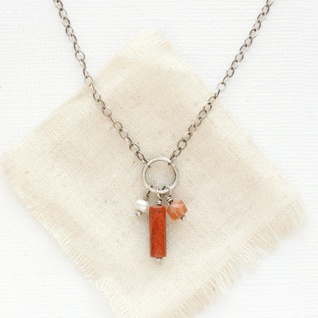 The pear, red jasper, and sunstone charm necklace styled on tan linen.
