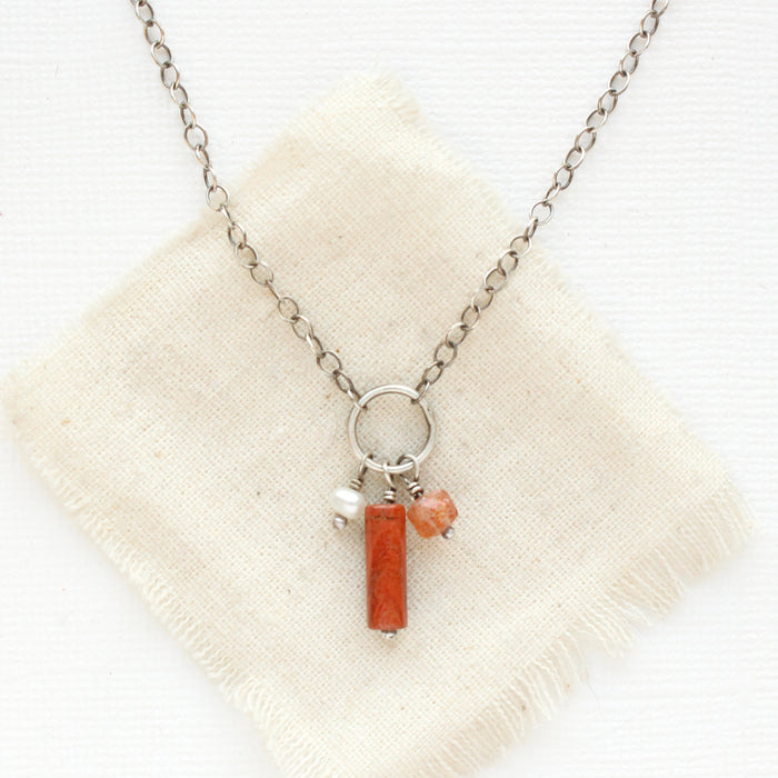 The pear, red jasper, and sunstone charm necklace styled on tan linen.