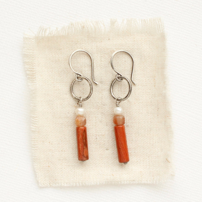The stacked pearl, sunstone, and red jasper hoop earrings styled on tan linen.