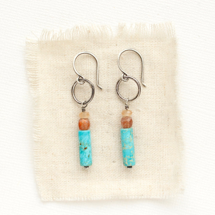 The stacked orange cat's eye quartz, sunstone, and sea sediment jasper hoop earrings styled on tan linen.