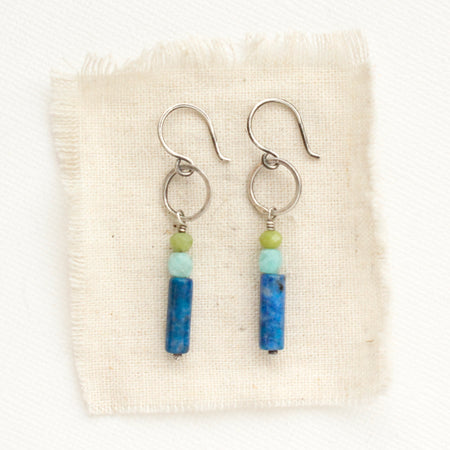 The stacked olivine jade, amazonite, and lapis lazuli hoop earrings styled on tan linen.