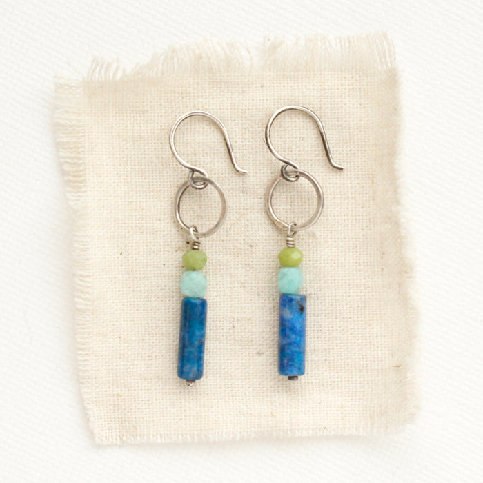 The stacked olivine jade, amazonite, and lapis lazuli hoop earrings styled on tan linen.