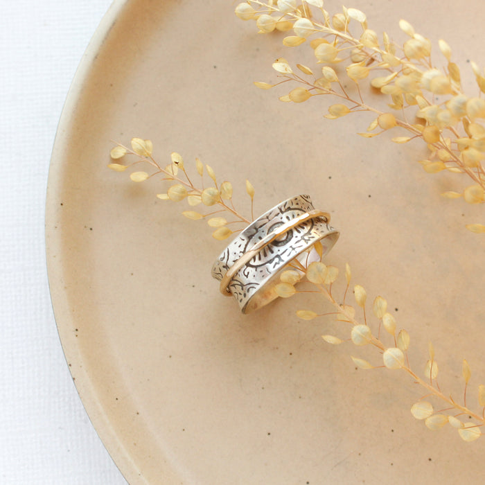 The mixed metal spinner ring styled on a tan plate with dried grass