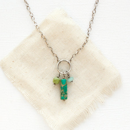 The green sediment jasper, olivine jade, and amazonite charm necklace styled on tan linen.