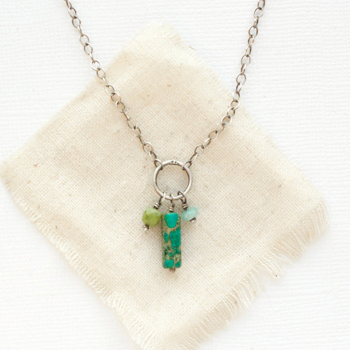 The green sediment jasper, olivine jade, and amazonite charm necklace styled on tan linen.