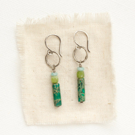 The stacked amazonite, olivine jade, and green sediment jasper hoop earrings styled on tan linen.