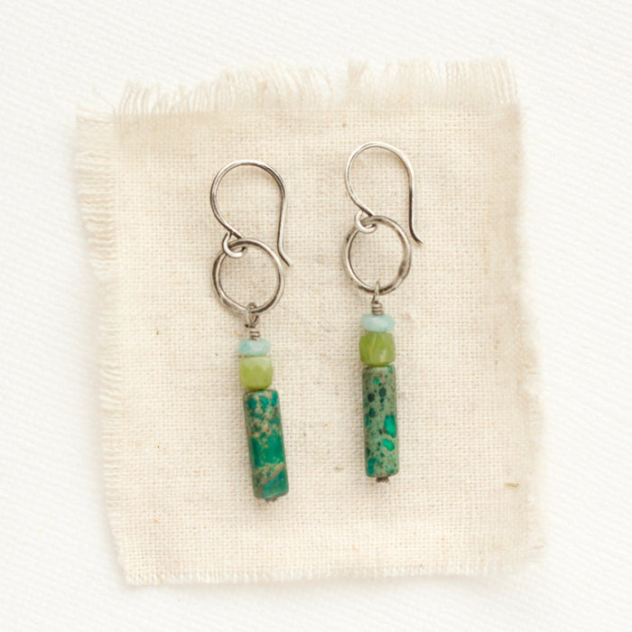 The stacked amazonite, olivine jade, and green sediment jasper hoop earrings styled on tan linen.