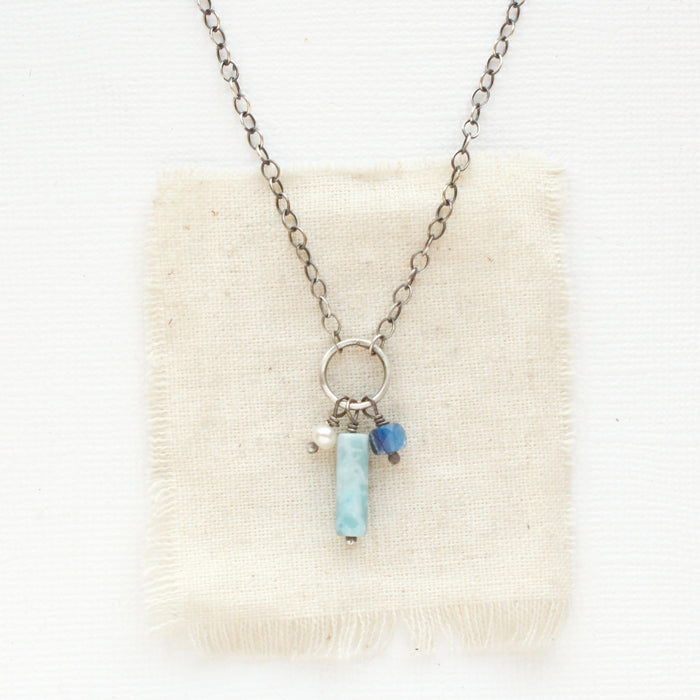 The larimar, pearl, and kyanite charm necklace styled on tan linen.