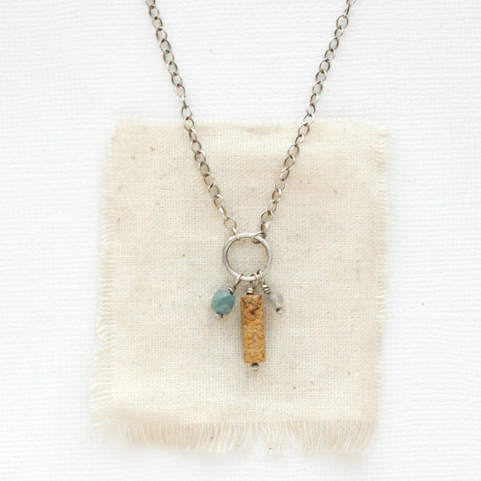 The kyanite, picture jasper, and labradorite charm necklace styled on tan linen.