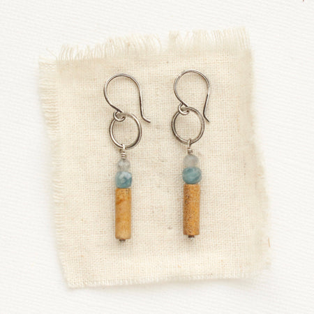 The stacked labradorite, kyanite, and picture jasper hoop earrings styled on tan linen.