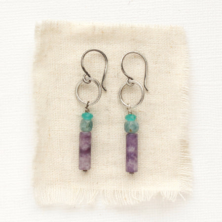 The stacked blue cat's eye quartz, kyanite, and lepidolite hoop earrings styled on tan linen.