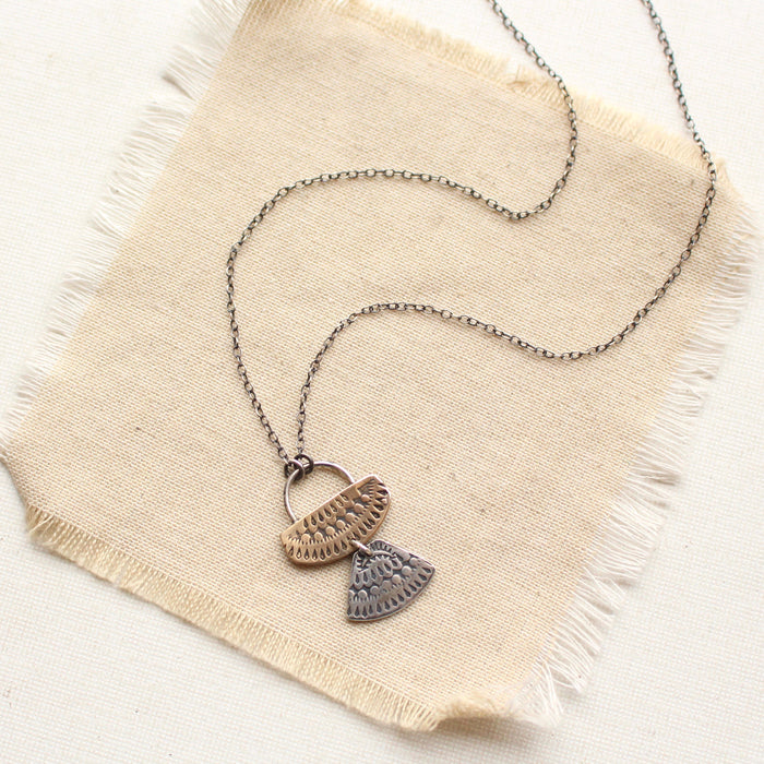 The stamped silver and bronze asmi duo necklace styled on tan linen