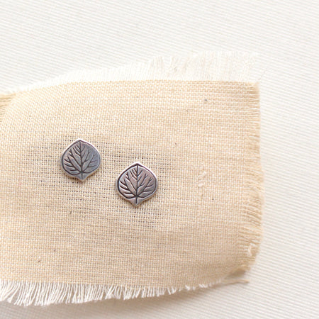 Stamped silver aspen leaf post earrings styled on tan linen