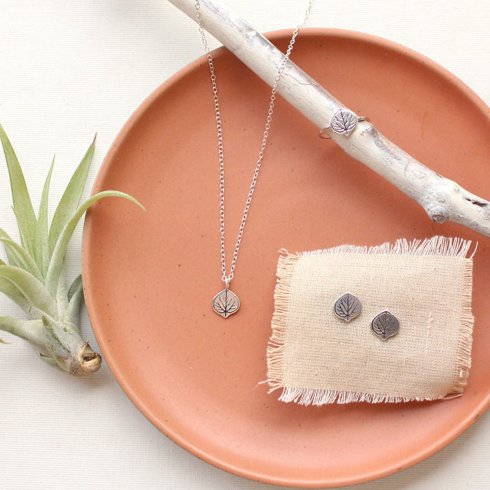 Stamped silver aspen leaf post earrings and necklace set styled on a red plate with an airplant and wooden stick