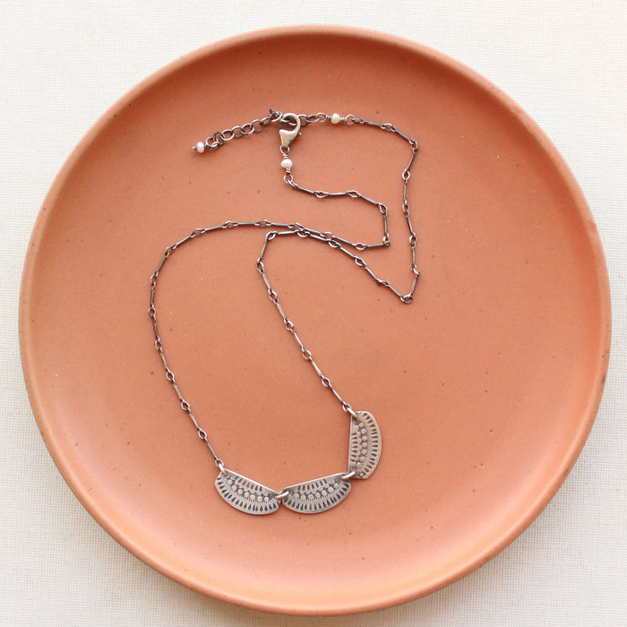 The asmi trio collar necklace styled on a red plate showing the adjustable clasp closure