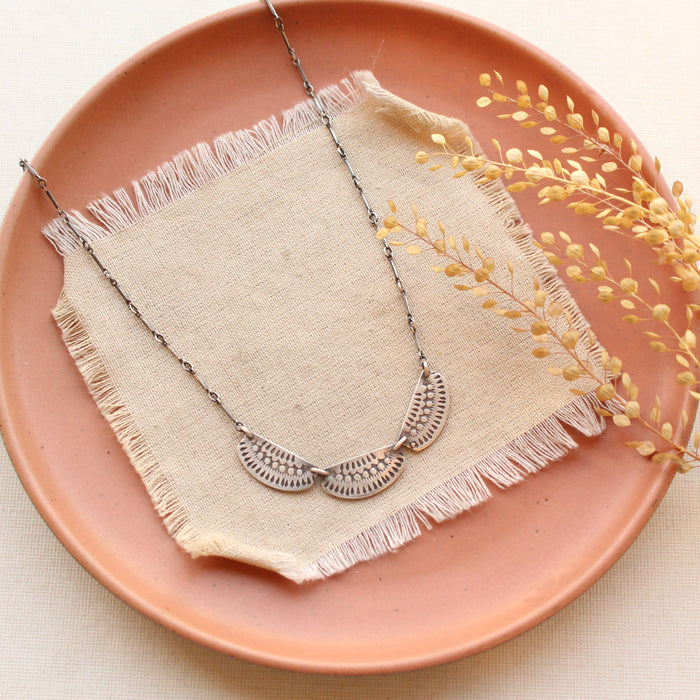 The asmi trio collar necklace styled on a red plate with linen and dried grass