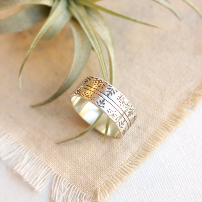 The nordic stamped band ring is styled on tan linen with an air plant