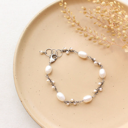 The wrapped pearl bud vine bracelet in silver styled on a tan plate with dried grass