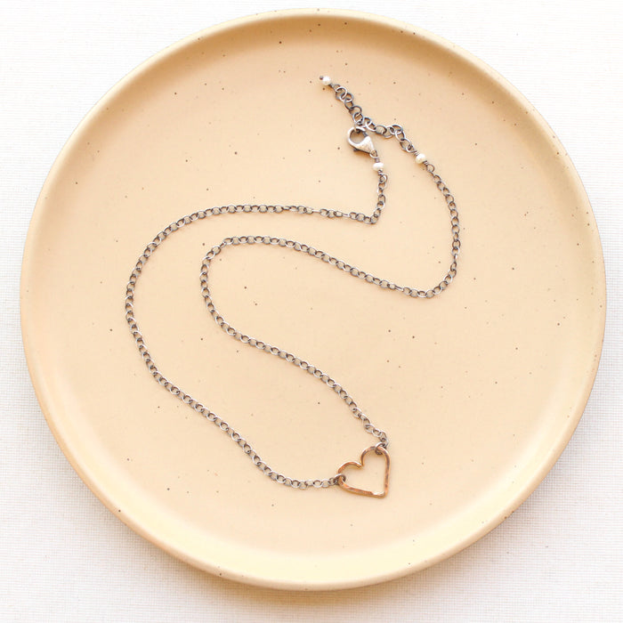 The mixed metal floating heart necklace styled on a tan plate showing the adjustable lobster clasp closure