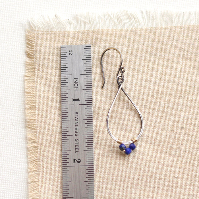 A lapis wrapped teardrop mixed metal hoop earring next to a ruler for size reference