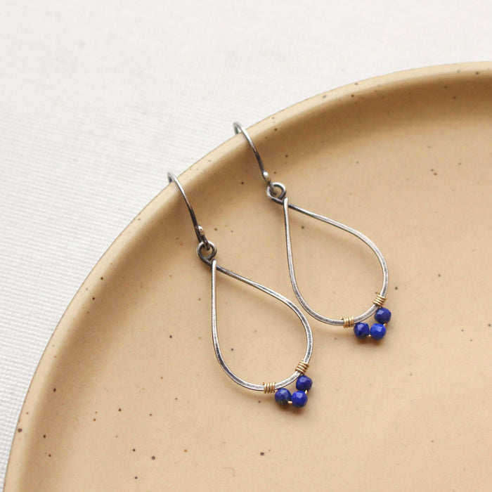 The southwest lapis wrapped teardrop mixed metal hoop earrings styled on a tan plate