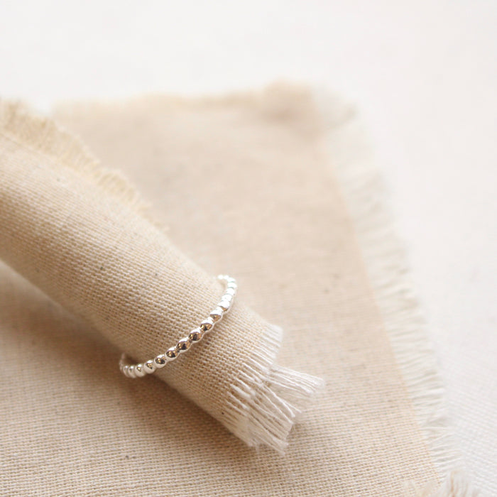 Sterling silver beaded stacking ring styled on tan linen