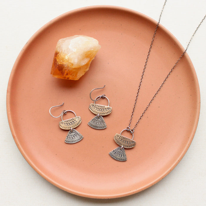 The stamped silver and bronze asmi duo earrings and necklace set styled on a red plate with a crystal