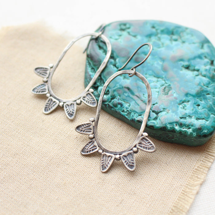 The tribal inspired feathered hoop earrings styled on tan linen with a blue stone