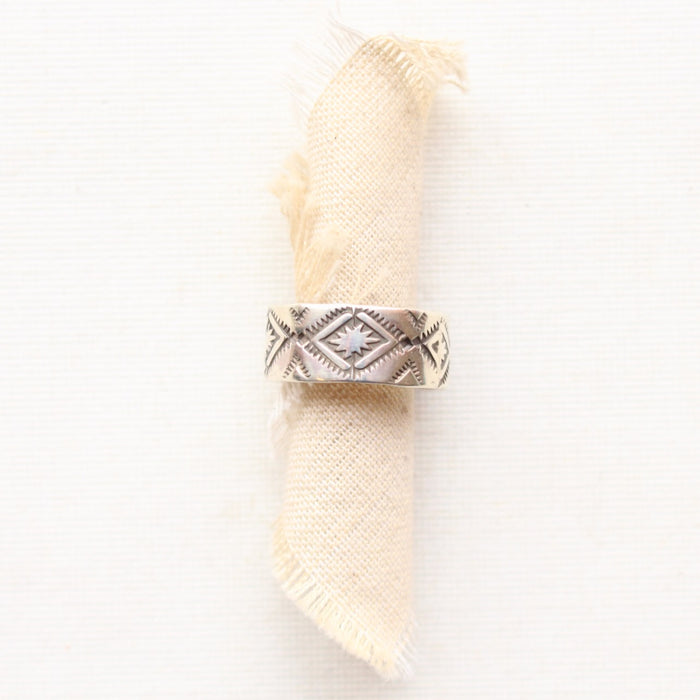 The stamped textile silver band ring is styled on a roll of tan linen