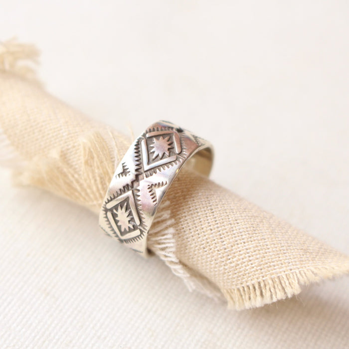 The stamped silver band ring is styled on a roll of tan linen