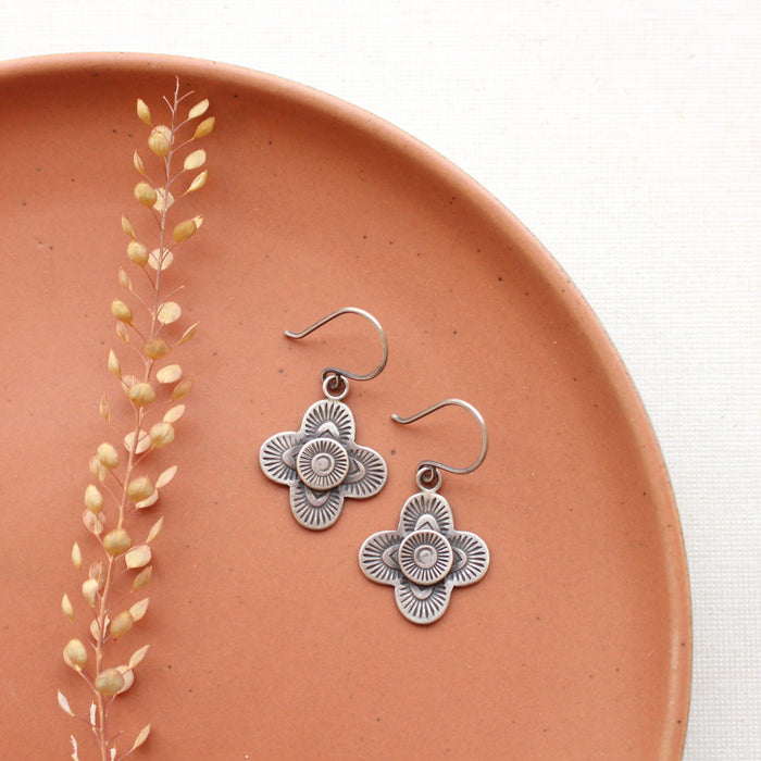 The stamped silver layered talara earrings styled on a red plate with dried grass