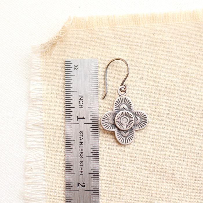 A stamped silver talara earring next to a ruler for size reference
